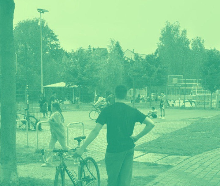 Ein Foto des Konkordiaparks, das grün eingefärbt ist. Im Vordergrund steht ein Junge mit seinem Fahrrad mit dem Rücken zum Betrachter. Im Hintergrund spielen Jugendliche Basketball.